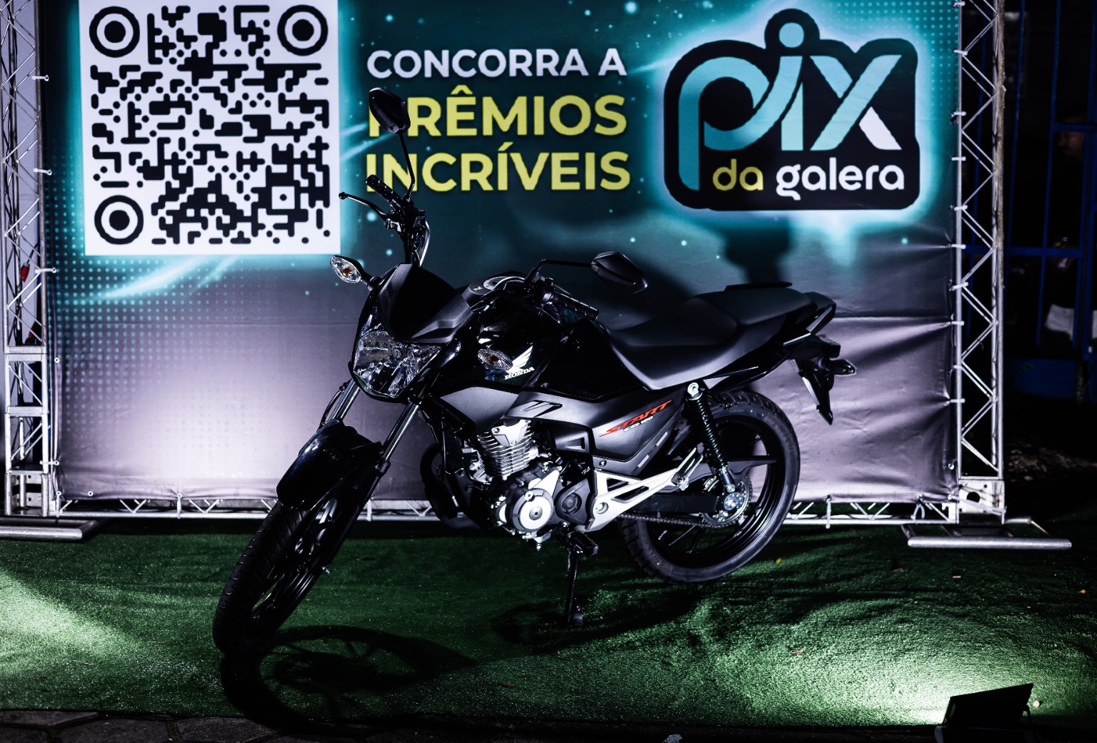 Motocicleta exposta diante do painel PIX DA GALERA, com QR code e chamada visual para prêmios.