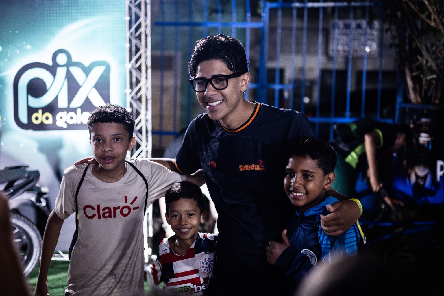 Participante posa com crianças diante do painel PIX DA GALERA.