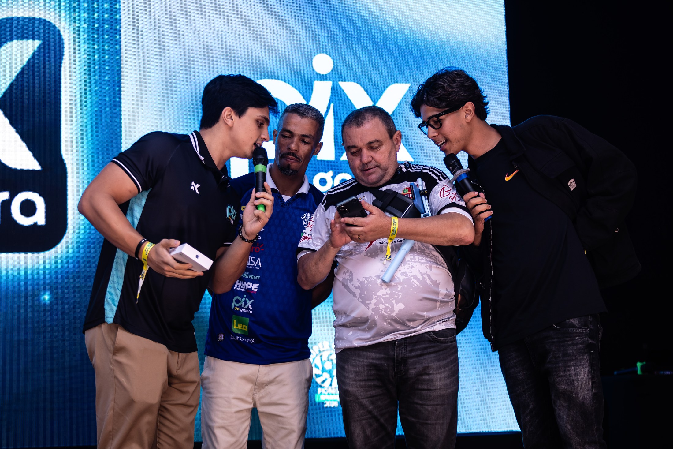 Participantes interagem em atividade de palco com comunicação PIX DA GALERA ao fundo.