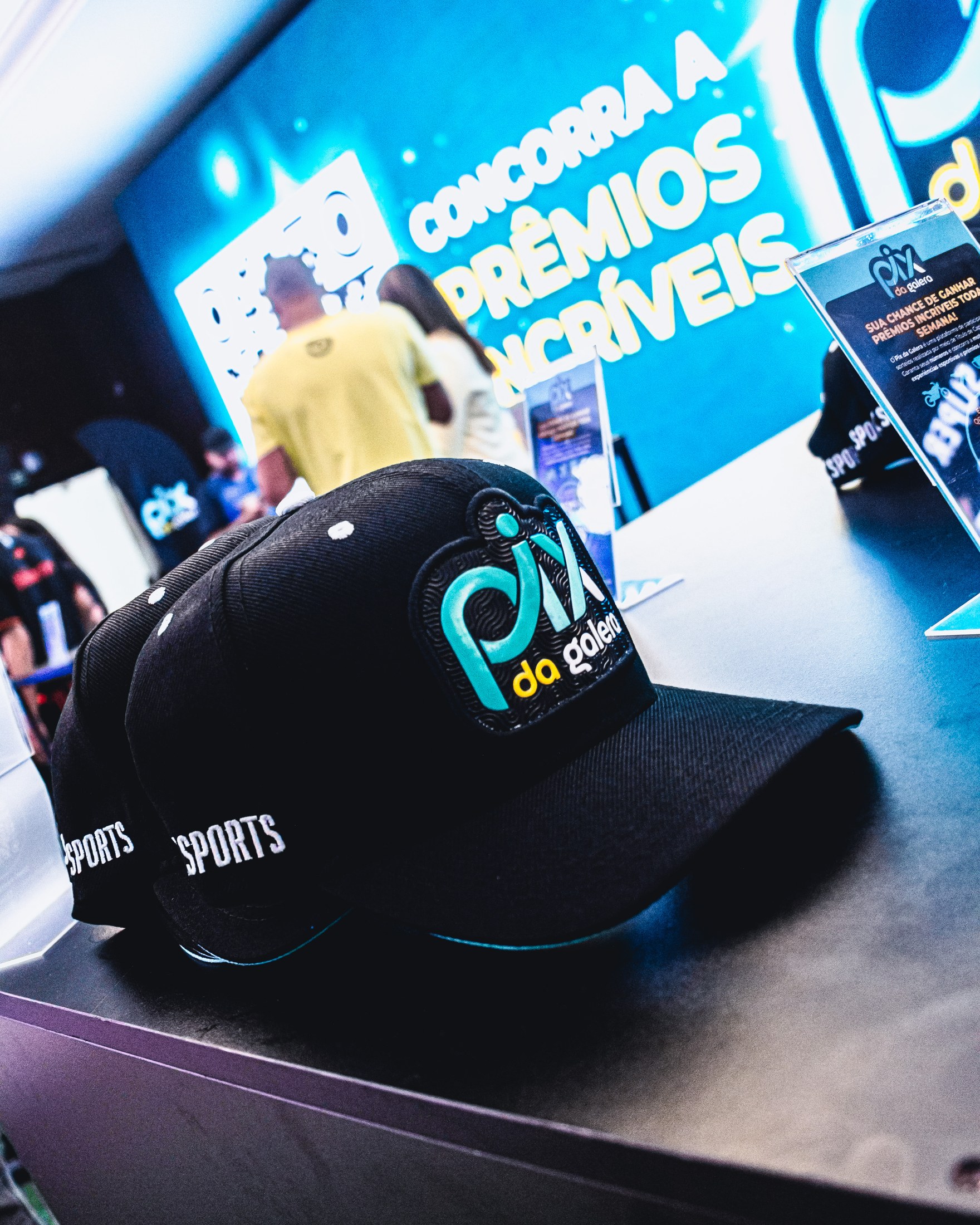 Boné e materiais com o logo PIX DA GALERA em mesa de ativação no congresso.