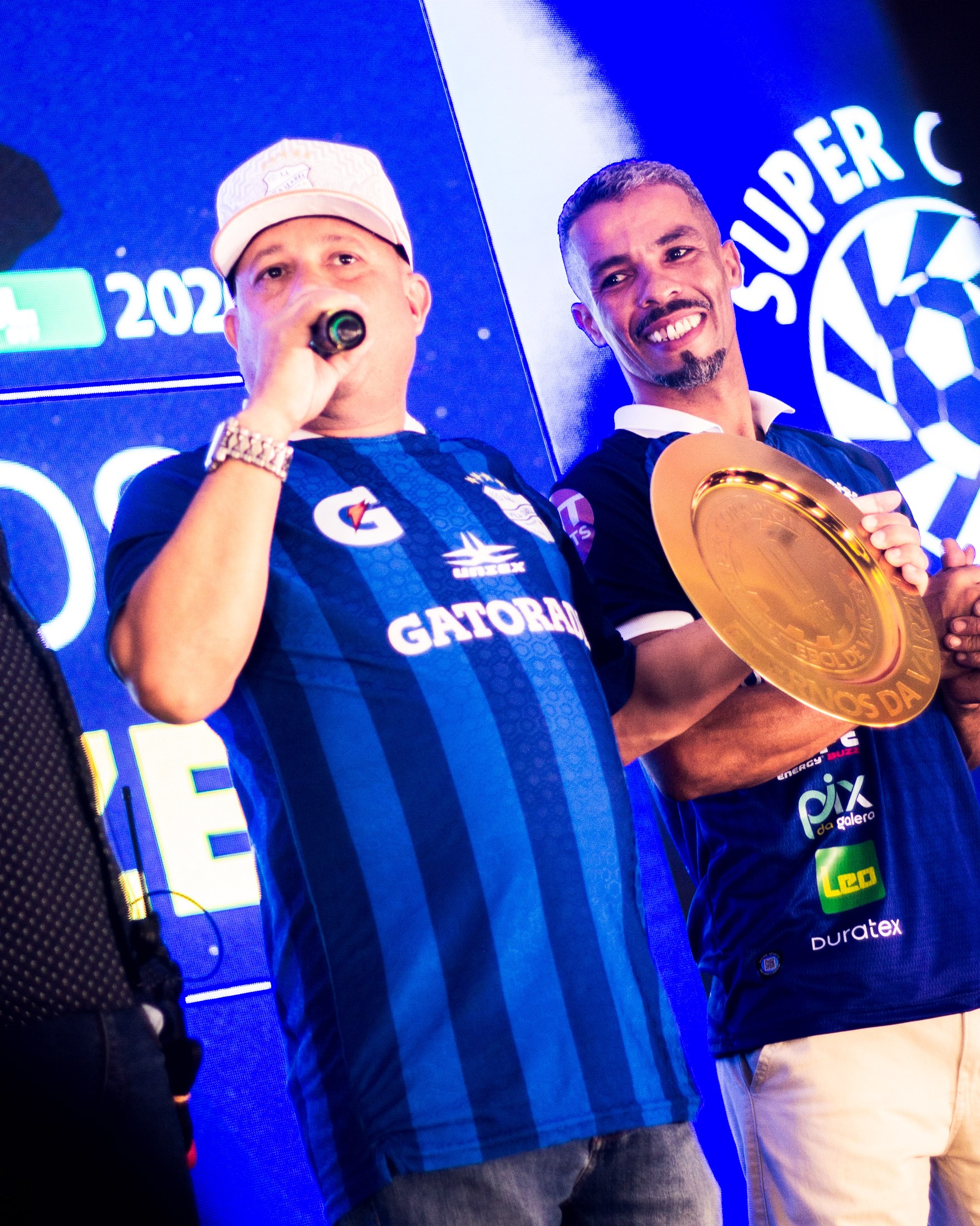 Apresentador e convidado exibem uma taça durante o evento com PIX DA GALERA visível.
