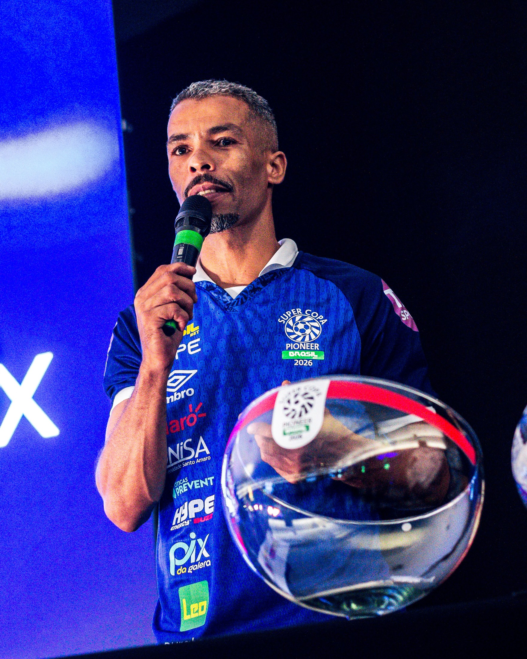 Convidado posa com material do evento usando camisa azul com PIX DA GALERA visível.