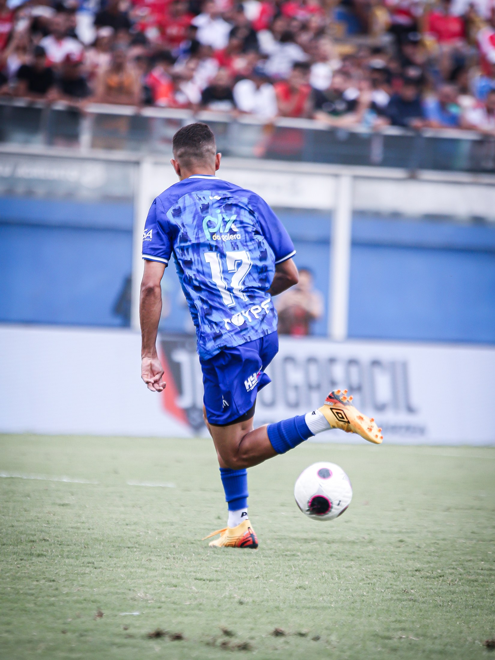 Jogador conduz a bola durante a final com PIX DA GALERA legível nas costas do uniforme azul.