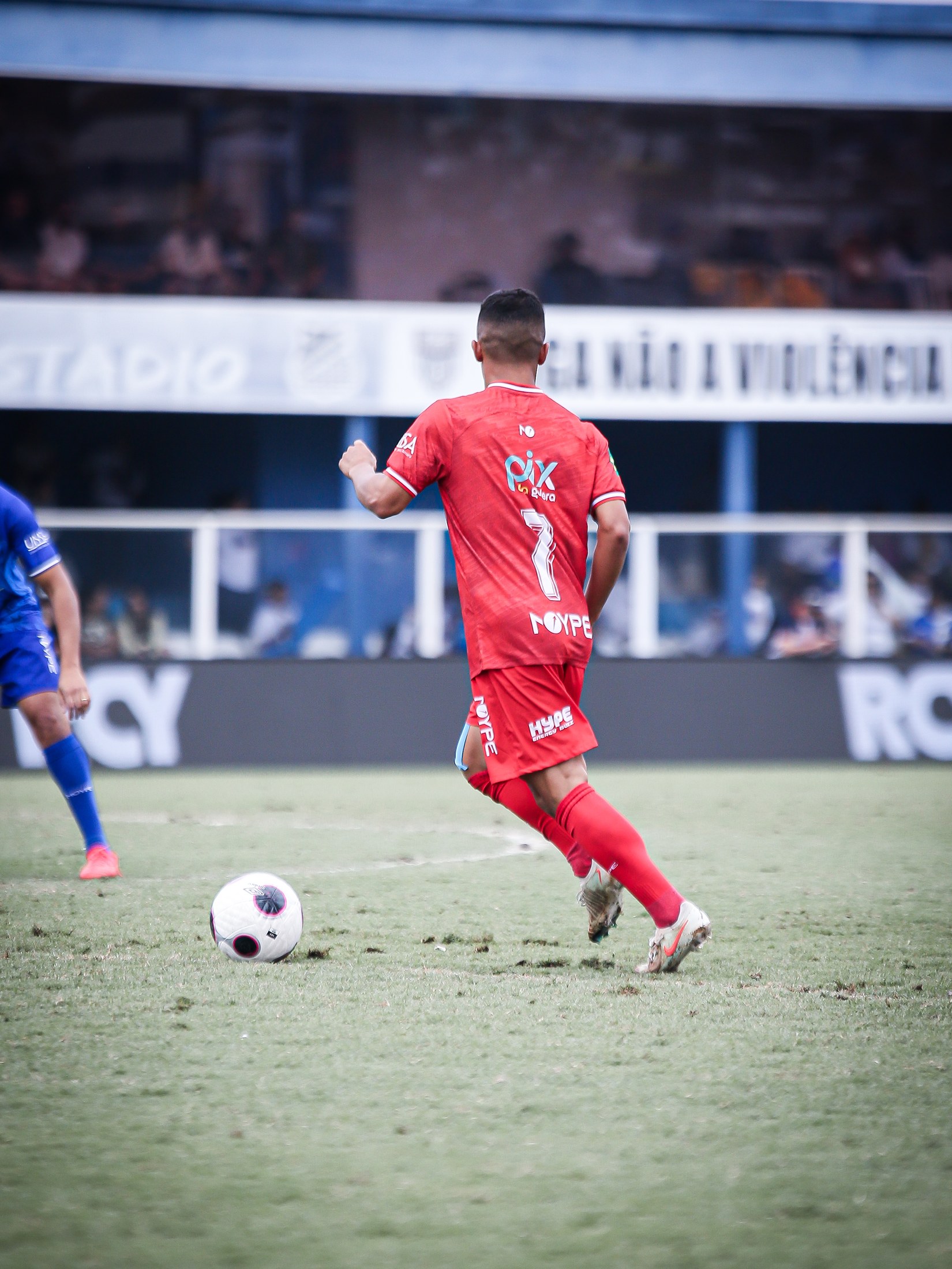 Atleta conduz a bola com o logo PIX DA GALERA visível nas costas do uniforme vermelho.