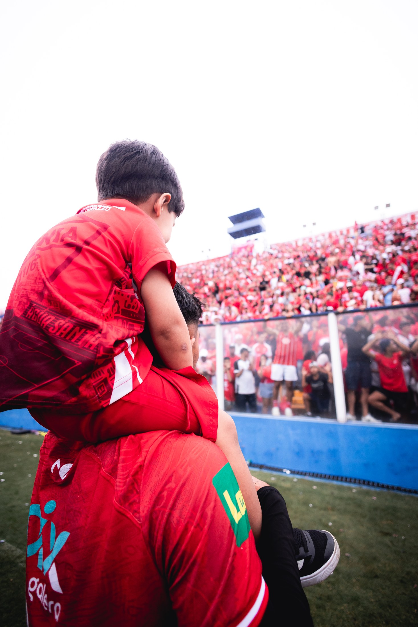 Torcedor mirim acompanha a partida sobre os ombros de um jogador; o logo PIX DA GALERA aparece na camisa.