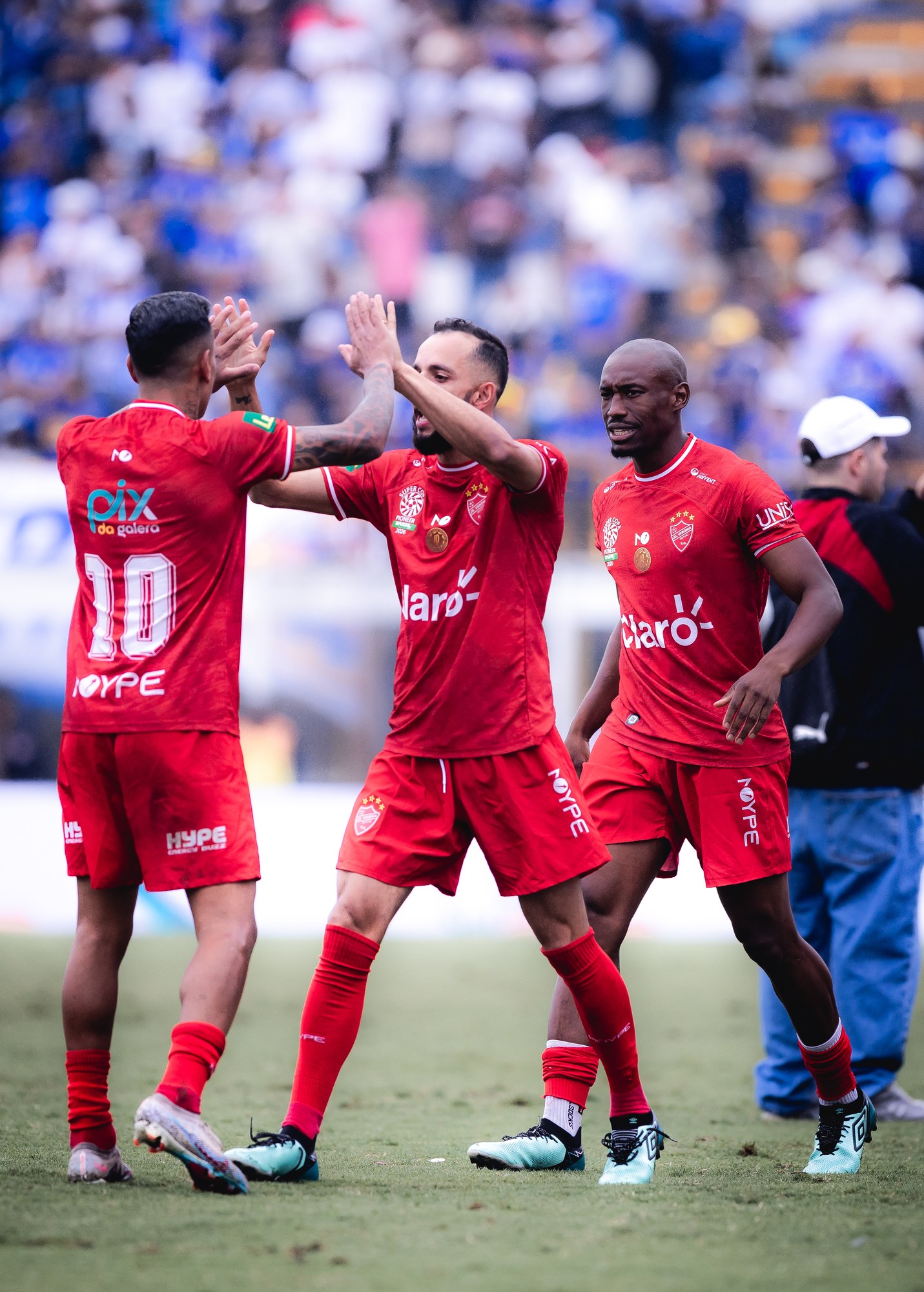 Jogadores trocam um cumprimento em campo; PIX DA GALERA aparece no uniforme vermelho.