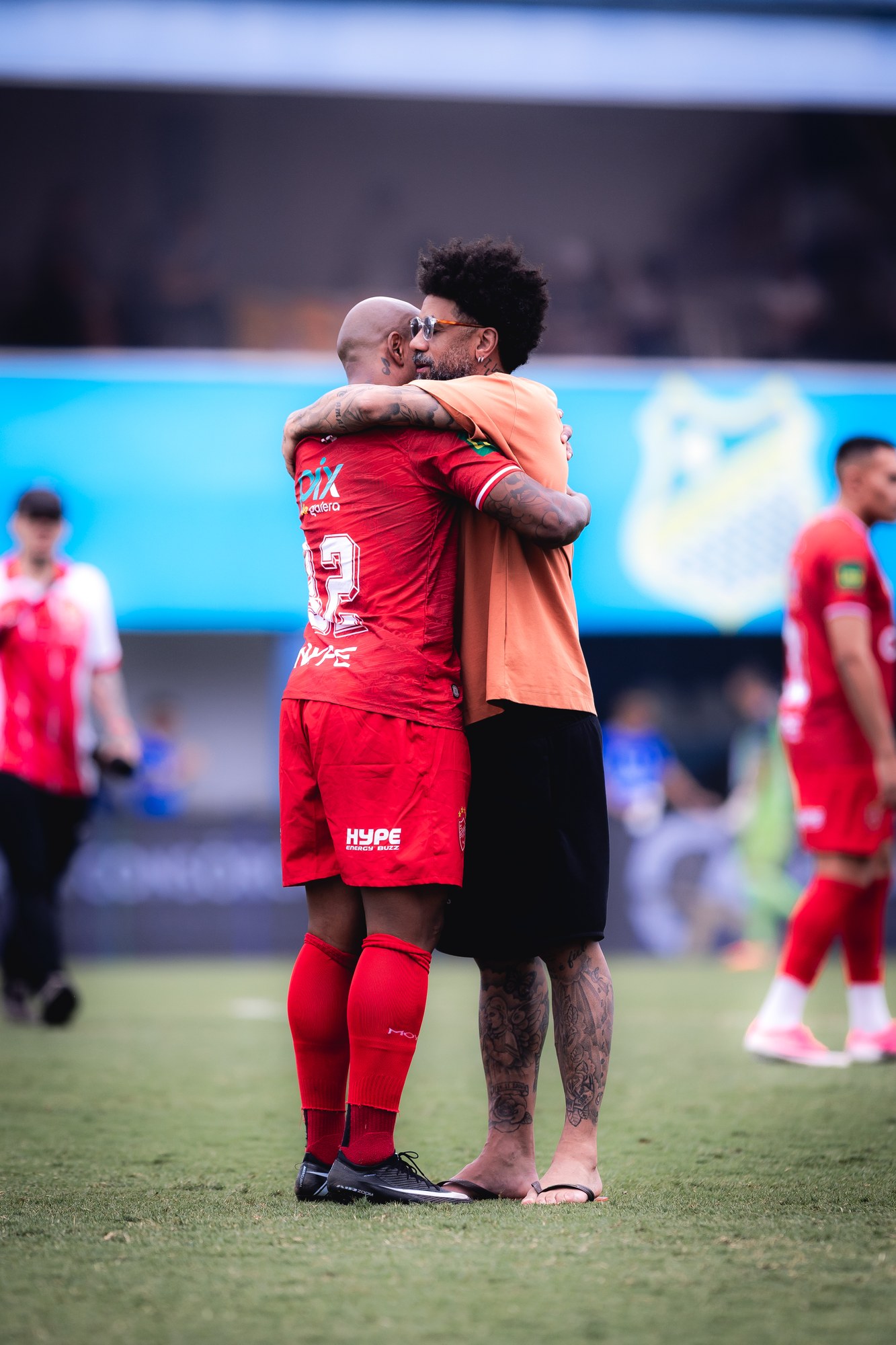 Jogadores se abraçam após um momento em campo; a marca está estampada no uniforme vermelho.