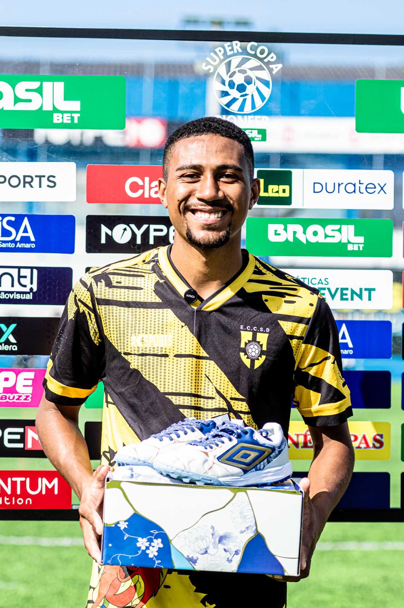 Jogador segura uma premiação diante do painel de parceiros da competição